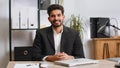 Indian business man sitting at office workplace desk closing laptop pc after finishing remote work Royalty Free Stock Photo