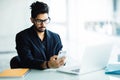 Young Indian CEO of company in his business office at desk, reading text on smartphone Royalty Free Stock Photo