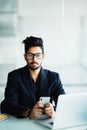 Young Indian CEO of company in his business office at desk, reading text on smartphone Royalty Free Stock Photo