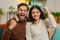 Indian couple celebrating success, clenching fists, showing thumbs up and giving high-five at home Royalty Free Stock Photo