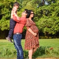 Indian couple posing for maternity baby shoot with their 5 year old kid. The couple is posing in a lawn with green grass and the