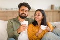 Indian couple sharing social media on cellphone, happy spouses sitting on sofa, using gadget, woman drinking coffee Royalty Free Stock Photo