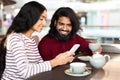 Indian couple with smartphone sitting on date in coffee shop Royalty Free Stock Photo