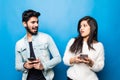 Indian couple typing on their phones looks each other isolated on blue background