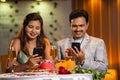 Indian couples at romantic candlelight dinner busy using mobile phone at restaurant - concept of social media sharing
