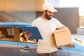Indian courier standing near his car holds parcel box outdoors
