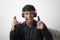 Indian cute teenager wearing black jacket, wireless headphone,holding cell phone,remote and keeping mouth open Royalty Free Stock Photo