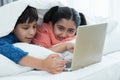 Indian family, brother and sister with traditional clothes smiling using laptop in bedroom at home, two children lying on bed Royalty Free Stock Photo