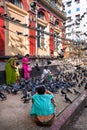 Indian family surrounded with pigeons. Two nearby vendors are ready to sell them pigeon food.