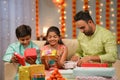 Indian father busy preparing gifts for diwali while spending time with siblings kids at home - concept of deepawali