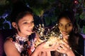 Indian female friends holding illuminated string lights in the evening