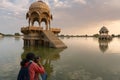 Indian female traveller, woman photographer taking picture of Chhatris and shrines with reflection of them on the water of Gadisar