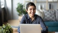 Indian freelance woman sitting near laptop laughing looking into distance