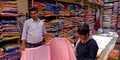 indian garment shopkeeper showing three piece outfits sari to female customer into the store