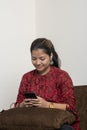 An indian girl using her mobile phone while sitting on a couch. Indian girl playing and using social media on her mobile phone. Royalty Free Stock Photo