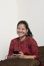 An indian girl using her mobile phone while sitting on a couch. Indian girl playing and using social media on her mobile phone. Royalty Free Stock Photo
