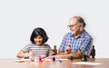 Indian grandfather helping grand daughter drawing & painting with colours and brush on paper at home Royalty Free Stock Photo