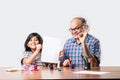 Indian grandfather helping grand daughter drawing & painting with colours and brush on paper at home Royalty Free Stock Photo