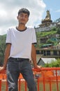 A Indian guy sitting on safety barrier by lake and beautiful hilly area of Tso-Pema and statue of Padmasambhava Guru Rinpoche