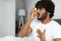 Indian guy suffering from asthma, using inhaler in bed Royalty Free Stock Photo