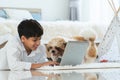 Indian handsome teenage boy lying on floor using laptop computer, relaxing playing with shih tzu dog puppy in bedroom at home. Pet