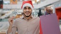 Indian happy Hispanic guy man in Santa X-mas Christmas hat in shopping mall looking camera showing holding money cash Royalty Free Stock Photo