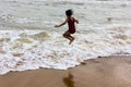 Indian kid girl jumping against approaching wave on puri sandy beach in seashore expressing joy and excitement Royalty Free Stock Photo