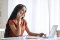 Indian lady using laptop, speaking on smartphone at home office Royalty Free Stock Photo