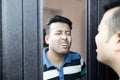 An indian male in casual t-shirt giving wierd expression at his reflection in mirror Royalty Free Stock Photo