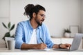 Indian male entrepreneur using laptop and taking notes while working in office Royalty Free Stock Photo