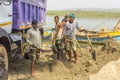 Indian male workers load sand into a truck with a spade