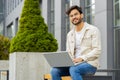 Indian man freelancer working on laptop computer sends messages reading email outdoors on bench Royalty Free Stock Photo