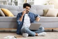 Indian man making phone call, drinking coffee and using laptop at home Royalty Free Stock Photo