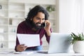 Indian man multitasking with phone and laptop while working at home office Royalty Free Stock Photo