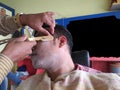 an indian man in pink shirt wearing yellow towel sitting on a chair in barber shop with eyes closed and foam applied for Royalty Free Stock Photo