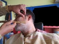 an indian man in pink shirt wearing yellow towel sitting on a chair in barber shop with eyes closed and foam applied for Royalty Free Stock Photo