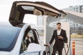 Indian man plugging in power cord to electric car