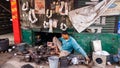 An Indian man sitting in his grungy pavement shop making metal utensils out of scrap m