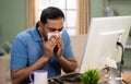 Indian man suffering from cold sneezing while working on computer at home - concept of Remote work, Health issues and Royalty Free Stock Photo