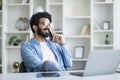 Indian man talking on cellphone while sitting at desk in home office Royalty Free Stock Photo