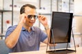 Indian man touch sunglasses leg and look to mirror also smiling during select best product in optical shop