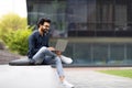 Indian man typing on laptop, sitting outdoor in urban area Royalty Free Stock Photo