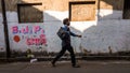 An Indian man walking past a grungy wall painted with political campaign of the