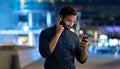 Indian man wearing earbud holding cell phone at night using smartphone.