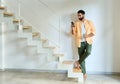 Indian man wearing earbud using smartphone standing at home.