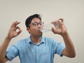 Indian man wearing glasses and a blue shirt showing okay gesture while drinking water