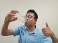 Indian man wearing glasses and a blue shirt showing okay gesture while drinking water