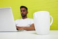 Indian man working at his desktop with mug in focus in foreground Royalty Free Stock Photo
