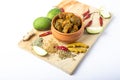 Indian mango pickle with green mango slices and spices with brown bowl on wooden board