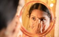 Indian married Woman applying Bindi, sindoor or decorative mark to forehead in front of mirror during festival